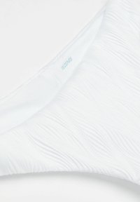 Bílé spodní díly bikin s texturovaným vlnitým vzorem, s měkkým povrchem. Obsahuje malé modré logo "Tezenis" na vnitřní straně.