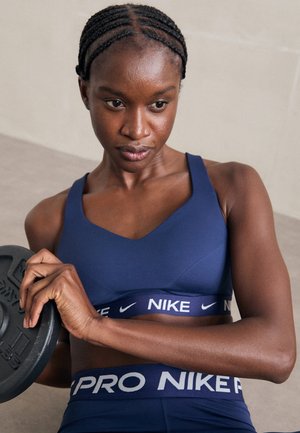 Kvinna i blått Nike träningskläder som håller en viktskiva, med fokus på styrketräning i en inomhusmiljö.