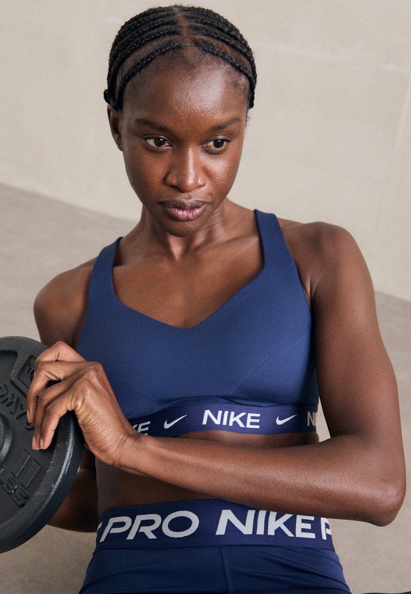 Kvinne i blått Nike treningsantrekk holder en vektplate, fokusert på styrketrening i en innendørs setting.