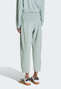 Jasnozielone spodnie dresowe o luźnym kroju i elastycznym pasie. Wykonane z teksturowanej tkaniny, z zwężanymi mankietami u dołu nogawek. Noszone z białymi trampkami.