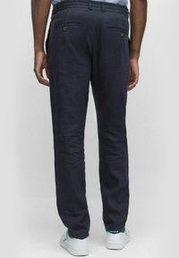 Marineblauwe linnen broek met een rechte pasvorm, voorzien van achterzakken met knoopsluiting; gedragen met witte sneakers. Geweldige textuur van de stof is zichtbaar.