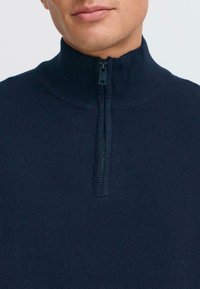 Maglione zip-up blu navy con colletto alto, texture a costine e una cerniera corta al collo, caratterizzato da un design semplice e uniforme.