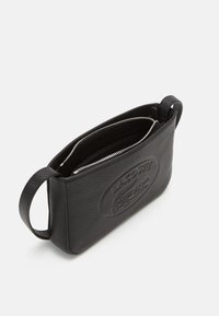 Sac en cuir noir avec une finition texturée, doté d'une fermeture éclair, d'un logo en relief sur le devant et d'une poignée latérale pour le transport.