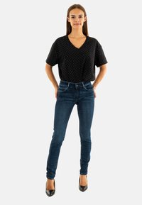 Top corto negro de manga corta con lunares blancos, combinado con jeans ajustados azul oscuro y zapatos de tacón negros. Diseño simple y limpio.