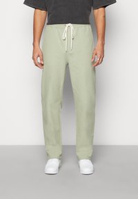 Pantalon vert clair, coupe décontractée, fabriqué en matériau doux. Comprend une ceinture élastique avec cordon blanc et des poches latérales.