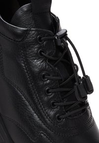 Sneaker alta nera in pelle con punta tonda, lacci elasticizzati e chiusure a toggle; presenta una texture liscia e dettagli cuciti.