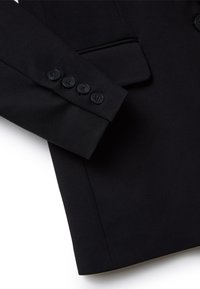 Giacca nera sartoriale con un tessuto liscio, forma strutturata e quattro bottoni neri sui polsini. Design minimalista senza motivi.