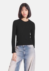 Czarna prążkowana bluzka z długim rękawem, dopasowana sylwetka i okrągły dekolt, zestawiona z jasnoniebieskimi, wyblakłymi jeansami o szerokich nogawkach.