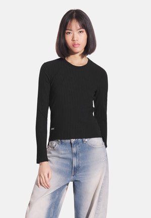 Czarna prążkowana bluzka z długim rękawem, dopasowana sylwetka i okrągły dekolt, zestawiona z jasnoniebieskimi, wyblakłymi jeansami o szerokich nogawkach.