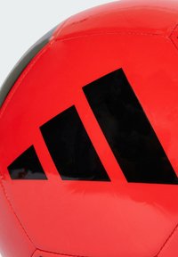 Pallone da calcio rosso con superficie lucida, caratterizzato da un prominente logo nero a tre strisce. Materiale leggermente texturizzato, forma rotonda, cuciture dettagliate.