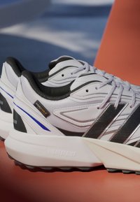 White athletic shoes with black accents, Cordura branding, textured mesh, and a prominent Lightstrike midsole. Blue and grey design detailing.