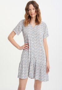 Vestido corto de mangas cortas en tejido ligero, con botones en la parte delantera y una falda en capas. Presenta patrones florales en azul, amarillo y naranja.