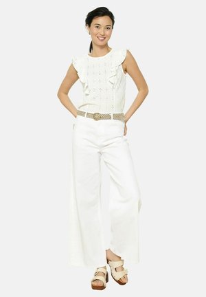 Haut blanc en broderie anglaise avec des volants, associé à un pantalon blanc à jambes larges. Ceinture tressée beige et sandales à plateforme crème avec des boucles.