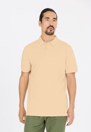 Beige kortærmet polo-shirt med en tre-knaps placket, glat tekstur og en afslappet pasform. Båret med grønne bukser.