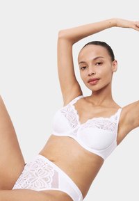 Vit spets-bh med prickar och vågiga kanter, kombinerad med matchande högmidjade trosor med spetsdetaljer och genomskinliga paneler.