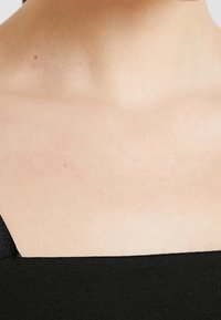 Top nero con scollatura quadrata, dotato di una texture liscia e opaca. Le spalline sono sottili e realizzate in un tessuto coordinato.