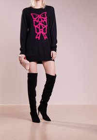 Musta neulemekko kirkkaan vaaleanpunaisella perhosgrafiikalla, jossa on pitkät hihat ja ribattu helma, yhdistettynä mustiin reiden ylle ulottuviin saappaisiin.
