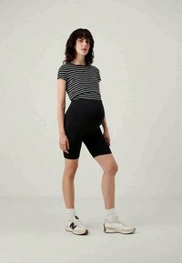 Shorts de cyclisme noirs associés à un t-shirt ajusté noir et blanc rayé. Modèle portant des baskets blanches avec des accents texturés. Fond neutre.
