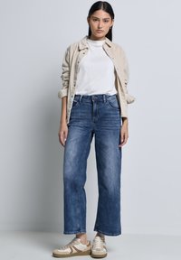 Lichtbeige corduroy shirt over een witte t-shirt, gecombineerd met hoge taille, wijde blauwe denim jeans en crèmekleurige sneakers. Soepele texturen, casual stijl.