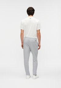 Ανοιχτό γκρι παντελόνι φόρμας με πλαϊνές τσέπες, ελαστική μέση και λευκά αθλητικά παπούτσια, σε συνδυασμό με κοντομάνικο λευκό t-shirt.