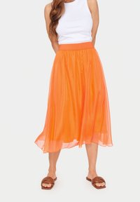 Orange, genomskinlig midikjol med elastiskt midjeband, som har en flödande design som skapar en mjuk silhuett. Tillsammans med bruna sandaler.