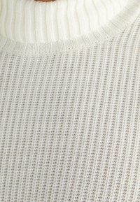 Kermanvärinen pooloneule, jossa on resoritekstuuri ja hienovarainen kuvio. Pehmeä neulottu materiaali ja istuva malli.