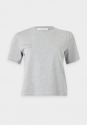 Le mannequin se tient devant un fond uni, vêtu d’un T-shirt gris, d’un pantalon foncé à jambes larges et de chaussures noires, avec un grand sac marron porté à l’épaule.