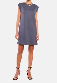 Szara sukienka na ramiączkach o luźnym kroju, wykonana z gładkiego materiału, z okrągłym dekoltem i delikatnym wykończeniem. W zestawie z czarnymi sandałami na obcasie.