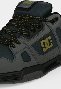 Gros plan d'une basket DC grise et noire avec un logo jaune et des lacets avec un motif noir et jaune.