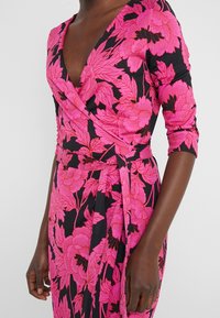 Langemouwige jurk met een diepe V-hals, met een zwarte achtergrond en een gedurfde roze bloemenpatroon. Wikkelontwerp met een strik in de taille.