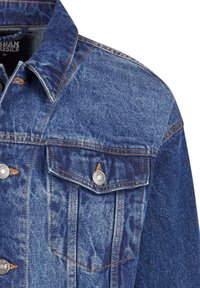 Partie supérieure d'une veste en denim bleu avec col pointu, boutons métalliques, poche poitrine à rabat et surpiqûres orange contrastantes.