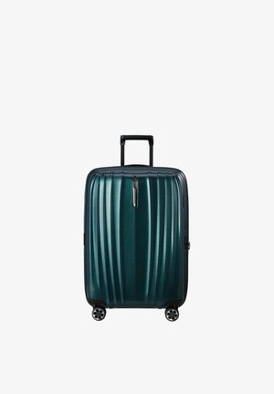 Valigia rigida verde petrolio scuro con manico telescopico e quattro ruote girevoli, in piedi su sfondo bianco.