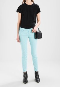 Camiseta negra de manga corta, jeans ajustados verde menta, bolso negro con detalles de tachuelas y botines negros de tacón con flecos decorativos.