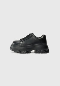 Black leather sneakers with a chunky sole, featuring a rounded toe, lace-up front, and textured ridges on the outsole for grip.