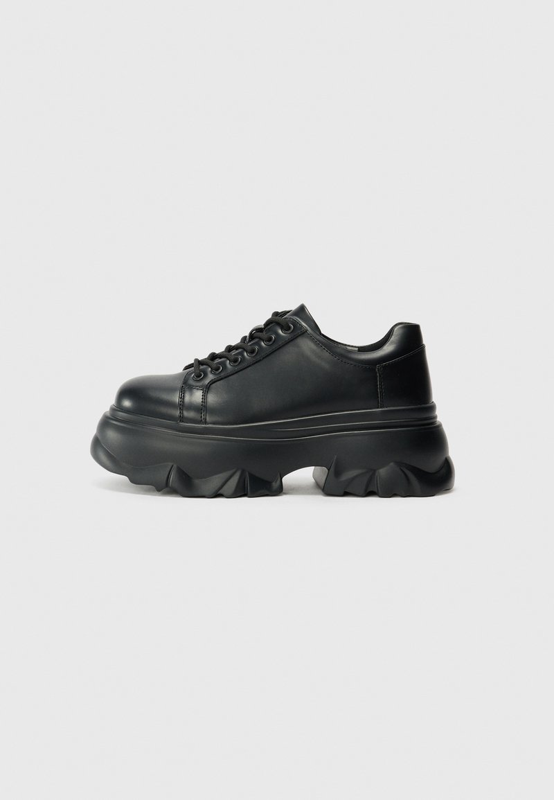 Black leather sneakers with a chunky sole, featuring a rounded toe, lace-up front, and textured ridges on the outsole for grip.