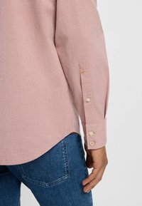 Lichtroze tekstuur shirt met lange mouwen, voorzien van knoopdetails op de manchetten, gecombineerd met blauwe denim jeans.