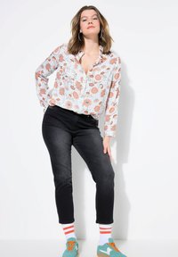 Camisa de manga larga floral con patrones en naranja y azul, combinada con jeans negros. El modelo lleva zapatillas de deporte en color azul verdoso y calcetines blancos con rayas naranjas.