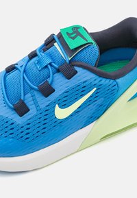 La chaussure de sport bleue présente une tige en mesh, des accents vert néon et une semelle blanche courbée avec des motifs texturés et un système de laçage sécurisé.