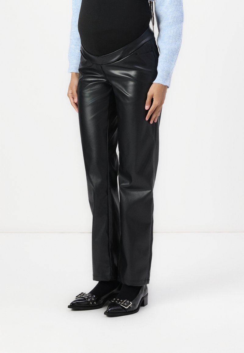 Pantalon en similicuir noir à taille haute, avec une texture lisse et une coupe à jambes larges. Associé à des chaussures noires à bout pointu.