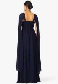Abito navy con schiena quadrata, corpetto arricciato e maniche a mantella fluenti. Realizzato in tessuto leggero con una consistenza morbida.