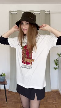 Λευκό T-shirt με πολύχρωμο γραφικό σχέδιο που απεικονίζει μια λεοπάρδαλη και τροπικά μοτίβα, συνδυασμένο με μαύρο φόρεμα με γιακά και σκούρο καπέλο καλοκαιρινής δαντέλας.