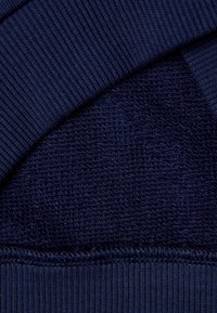 Tmavě modrá látka s texturovaným, měkkým povrchem přerušeným hladkým, žebrovaným okrajem, který zdůrazňuje kontrasty v materiálu a textuře.