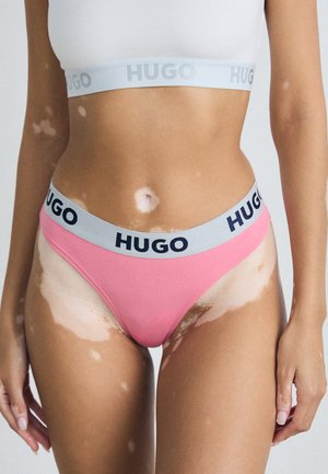 Rosa truse med grå HUGO liv, med marineblå tekst. Glatt stoff, høy-kuttet design, minimal dekning og ingen synlige mønstre.