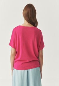 Fuchsia roze kortarmige top gemaakt van zacht materiaal, met een ruime halslijn en een ontspannen pasvorm, gecombineerd met lichte blauwe plooipantalons.