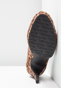 Chaussure à talons hauts imprimé léopard avec bout pointu, semelle noire embossée du texte répété « Tamaris ».