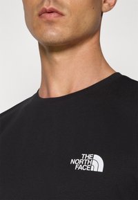 Tricou din bumbac negru cu guler rotund, având un logo alb "The North Face" pe partea stângă a pieptului. Textură netedă.