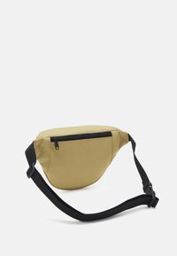 Bolso de cintura de tela beige con bolsillo frontal con cremallera y correa negra ajustable, aislado sobre un fondo blanco.