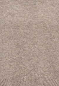 Gros plan d'un tissu tricoté beige montrant une texture fine de laine avec un motif côtelé en bas.