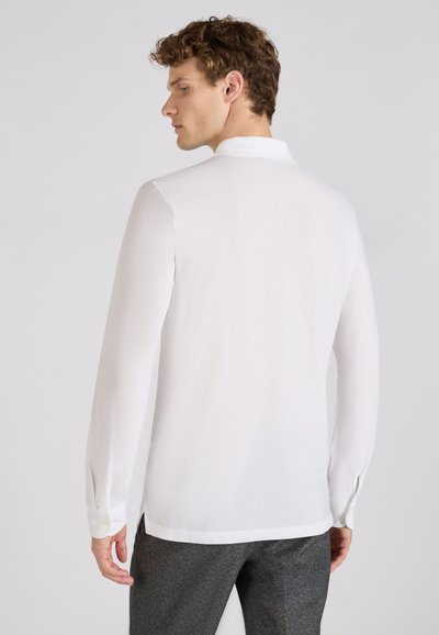 Witte langwerpige blouse met een klassieke kraag, gladde textuur en knoopmanchetten, gecombineerd met grijze textuurbroek.