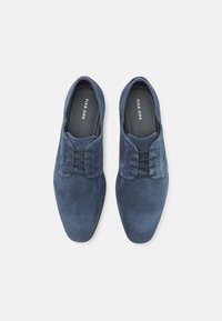 Zapatos de ante con cordones en azul oscuro, que presentan una textura suave, punta redondeada y cordones en tono. Logotipo impreso en la plantilla.